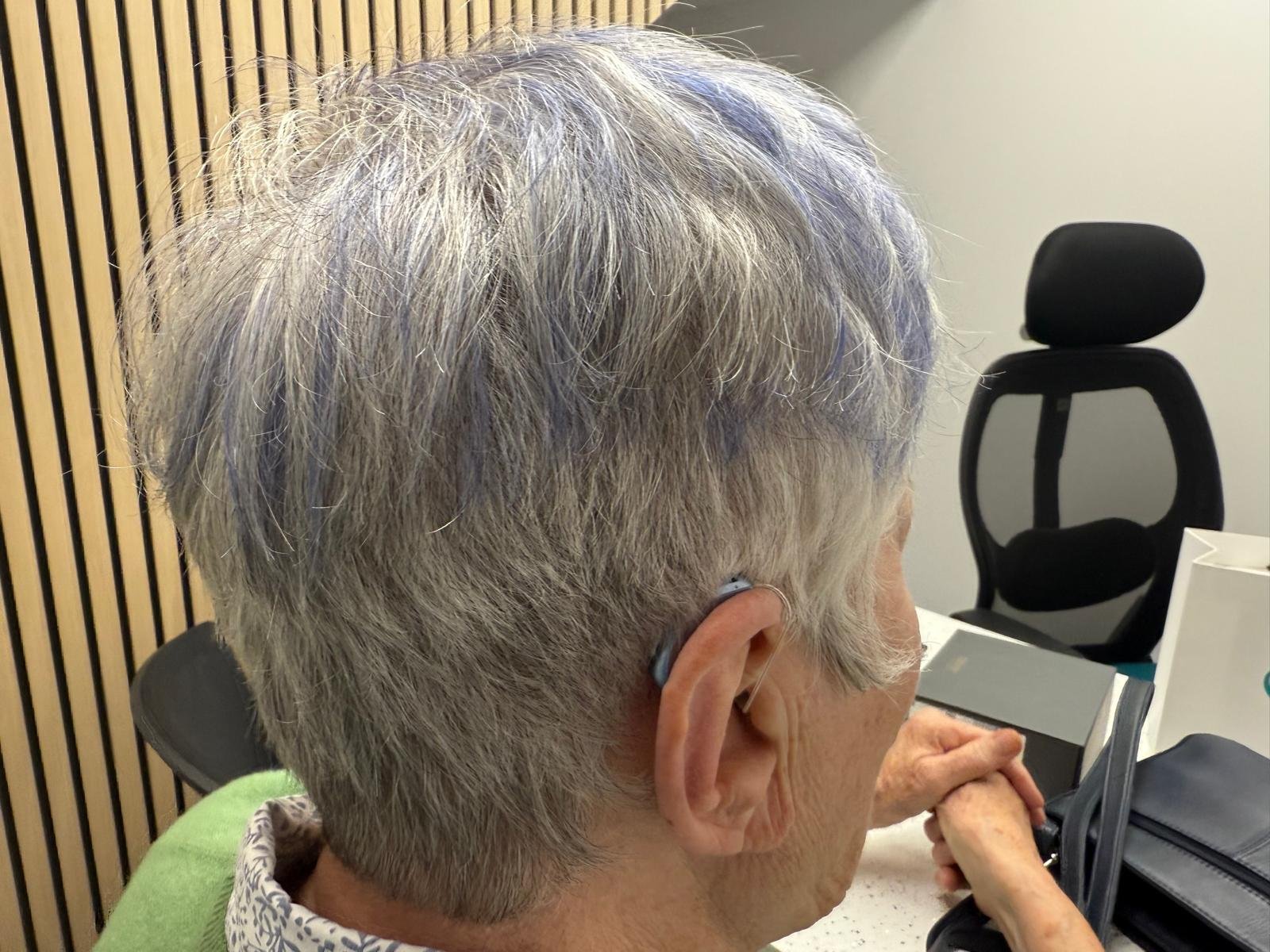 Patient wearing bright sky-blue hearing aids from behind