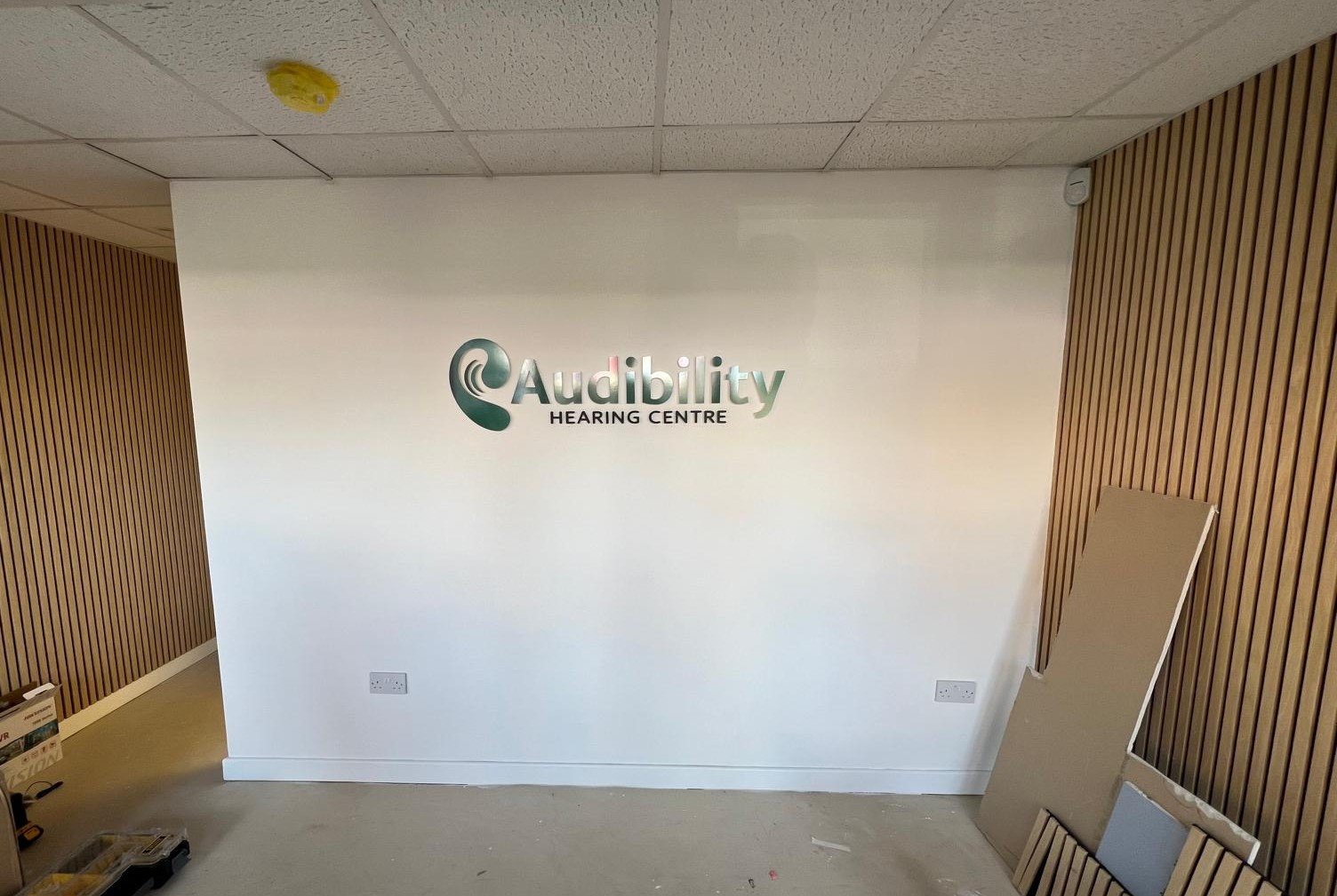 Audibility Hearing Centre signage being installed during the September 2024 clinic build, with construction materials visible as the space takes shape.